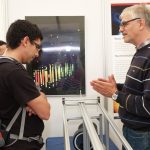 Prof. Lutz Köpke erklärt einem interessierten Besucher ein Neutrinoereignis, gemessen am IceCube Experiment am Südpol. Das Poster im Hintergrund zeigt das Ereignis.